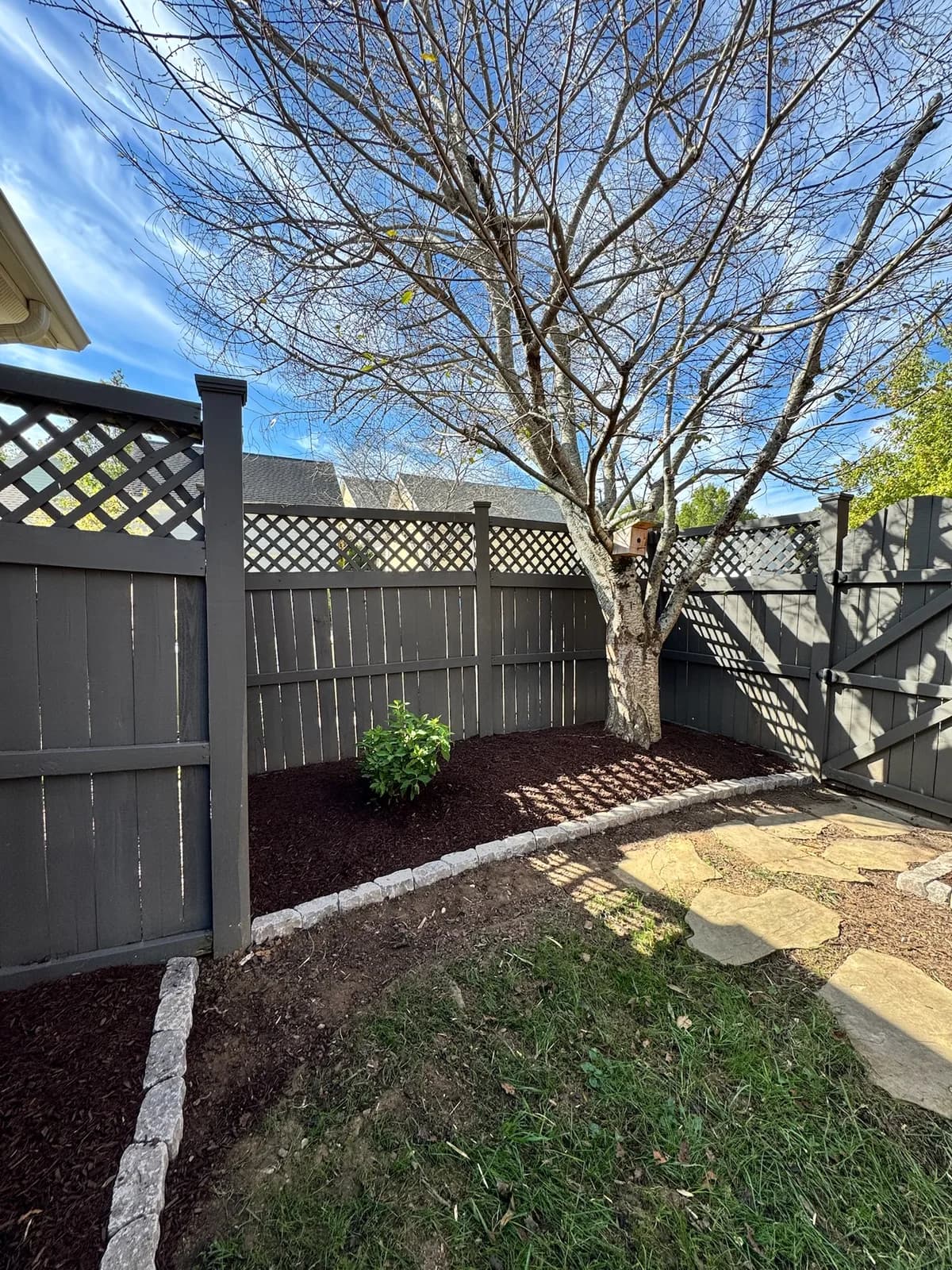 Curved mulch bed with cobble edging along a privacy fence