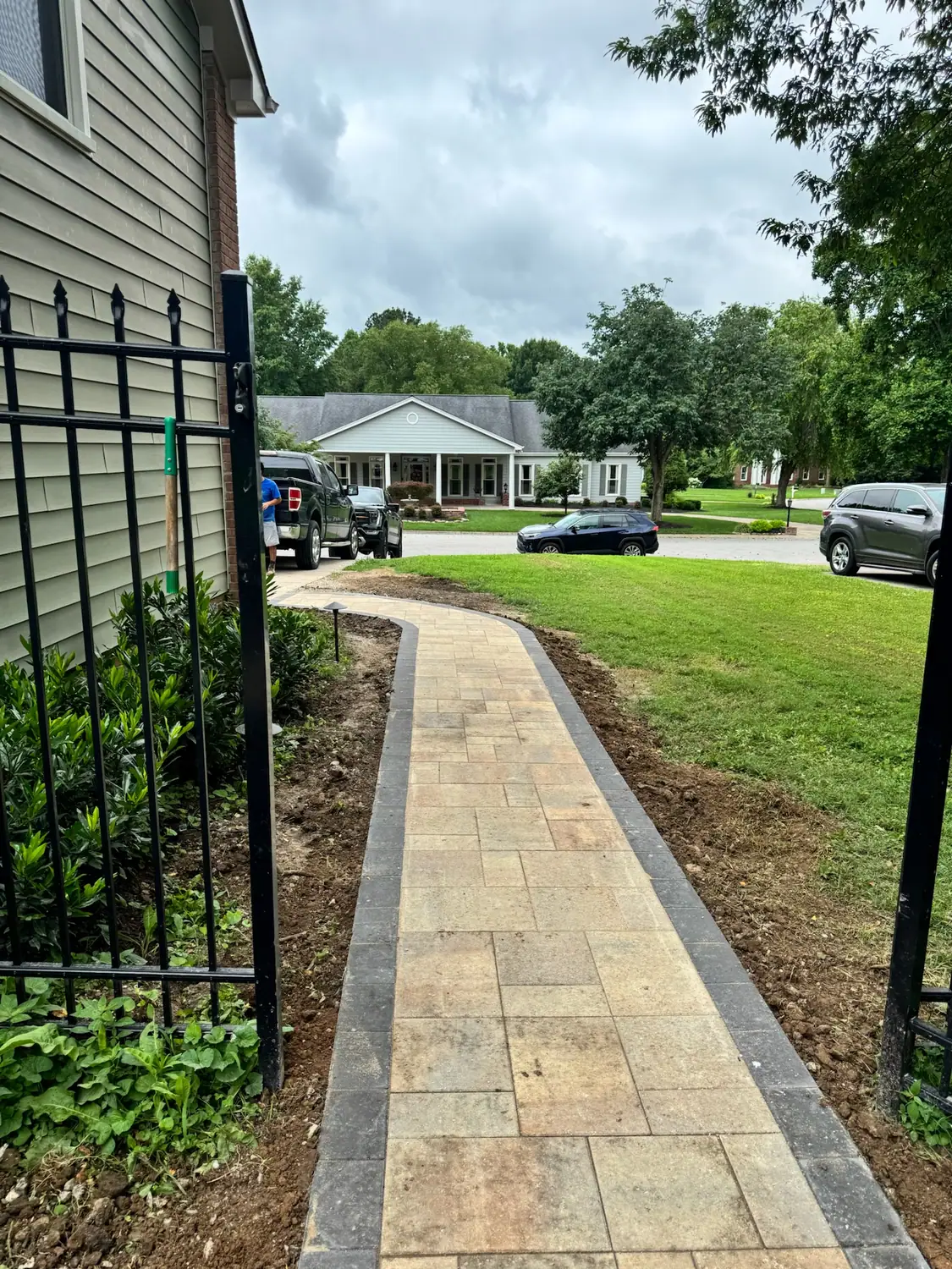 Paver walkway through a side yard beside an iron fence